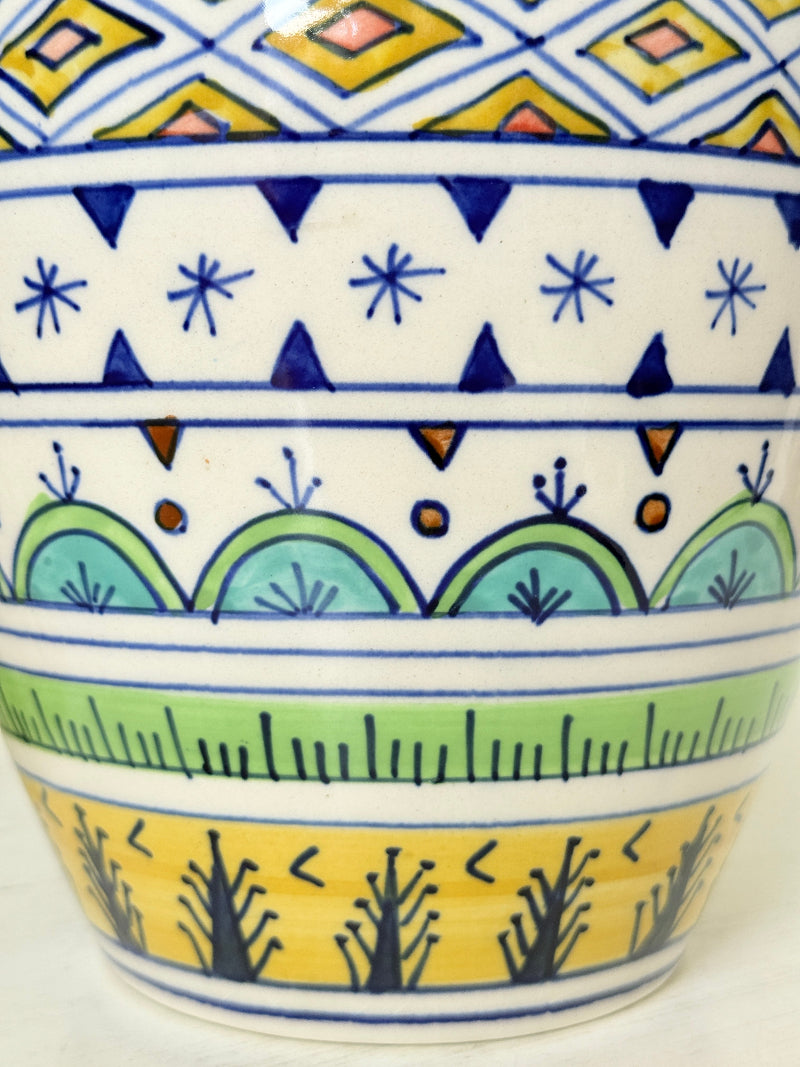 Close-up of a hand-painted ceramic cup featuring colorful geometric and botanical patterns in blue, green, yellow, and white.