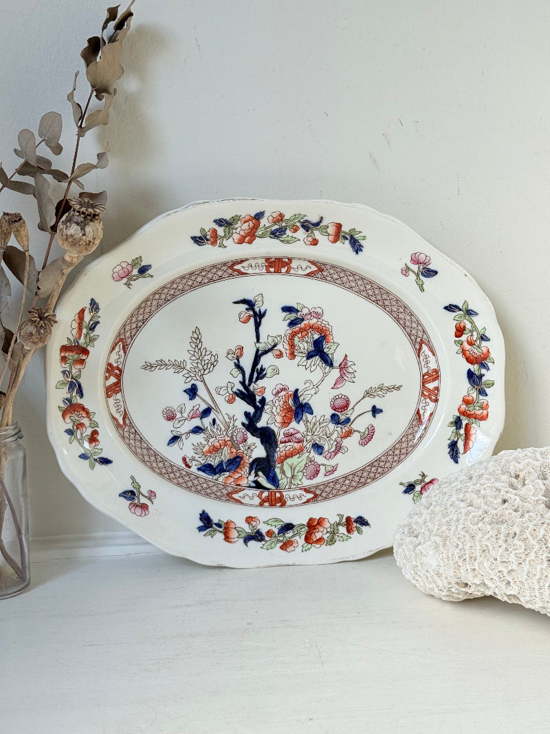 Vintage oval serving platter with chinoiserie style blue and red pattern photographed on a white surface