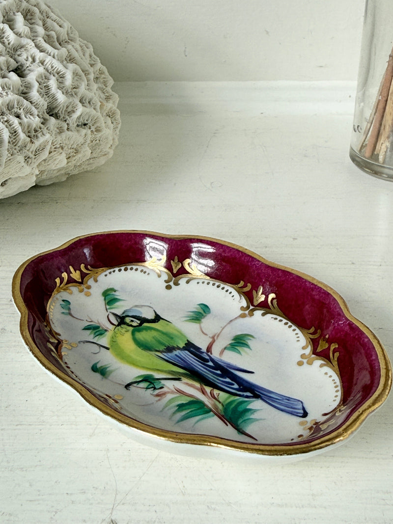 Vintage hand painted bird trinket dish with pink border and gilt detail photographed on a white surface