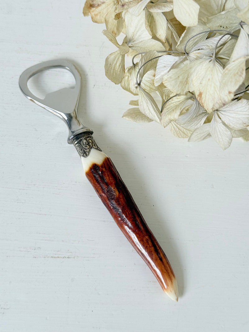 vintage antler handle bottle opener with stainless steel top photographed on white surface