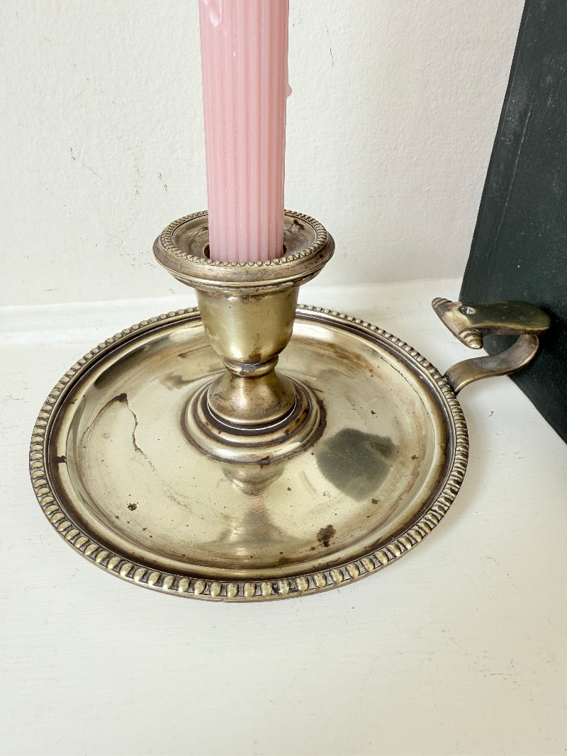 Antique silver plate chamberstick with handle, photographed on a white surface beside pink hydrangeas and vintage books