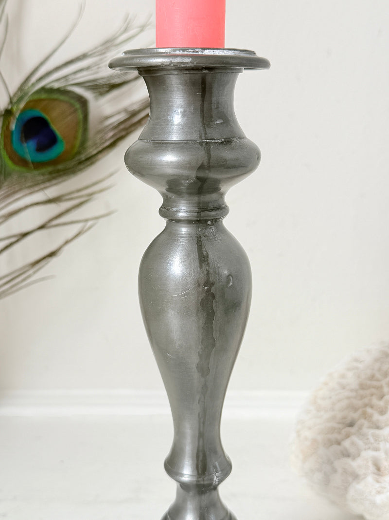 Antique pewter candlestick with baluster stem and aged patina styled with coral candle on white surface