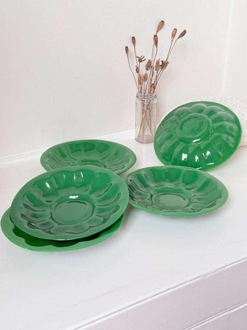 set of five vintage green pressed glass plates with decorative pattern, photographed on a white surface with dried flowers