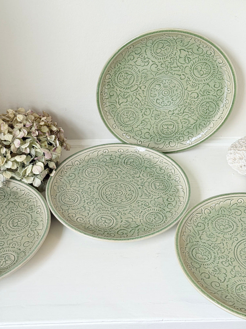 Set of four large Thai celadon stoneware plates in soft green glaze with raised pattern, photographed on a white surface