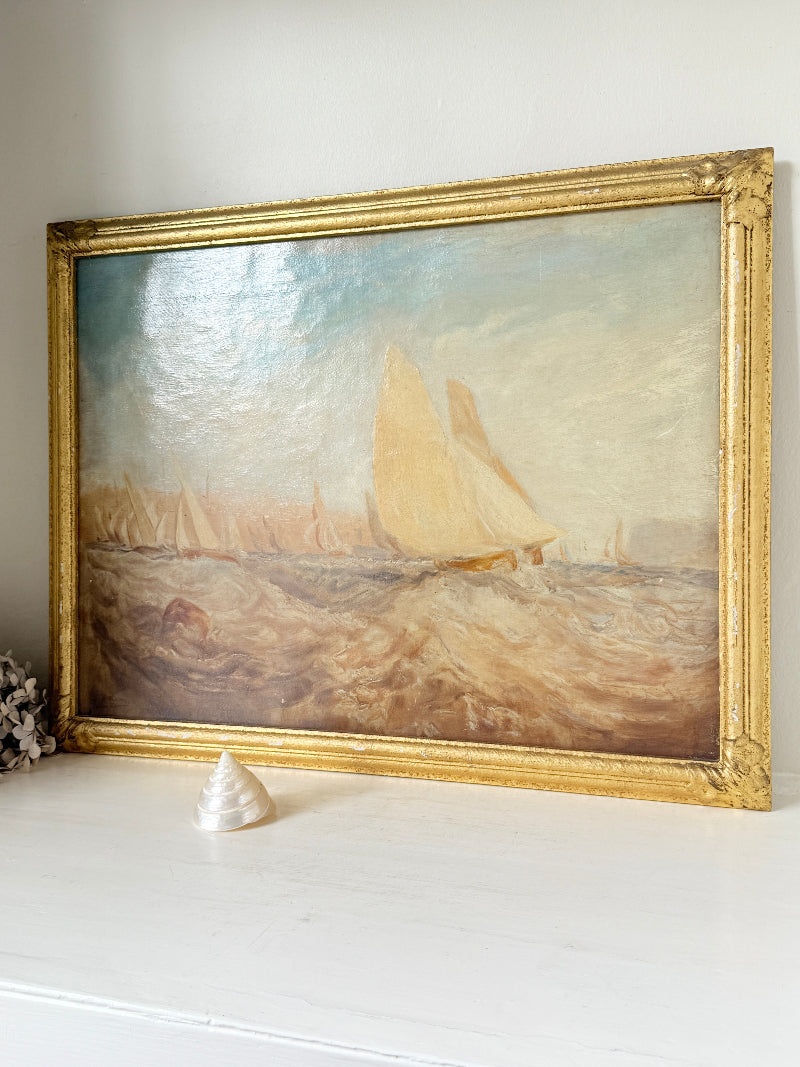 A framed oil painting of a sailing yacht on choppy water, housed in an ornate gold frame and displayed on a white mantelpiece.