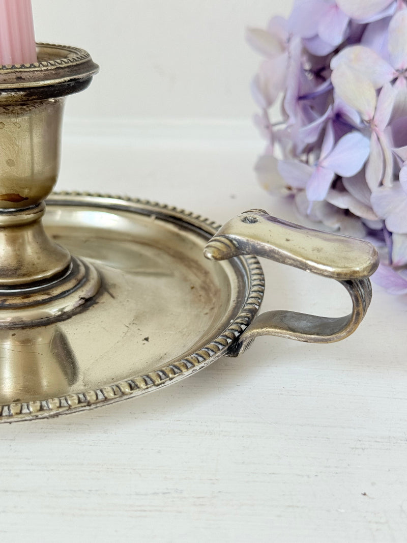 Antique silver plate chamberstick with handle, photographed on a white surface beside pink hydrangeas and vintage books