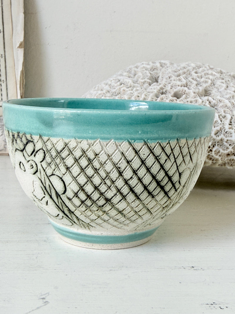 Hand thrown studio pottery bowl with turquoise glaze and hand decorated giraffe photographed on a white surface