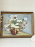 Vintage oil painting on board of daisies in a vase, framed under glass and photographed on a white surface beside dried flowers.
