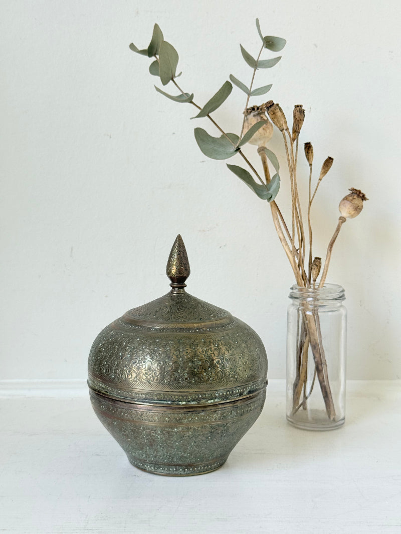 Indian Benares brass lidded jar with floral engraving and finial, photographed on a white surface