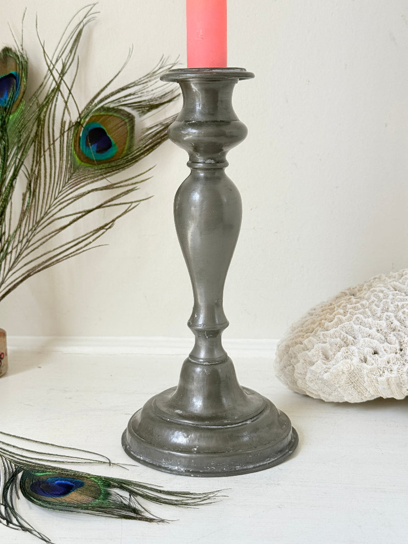 Antique pewter candlestick with baluster stem and aged patina styled with coral candle on white surface