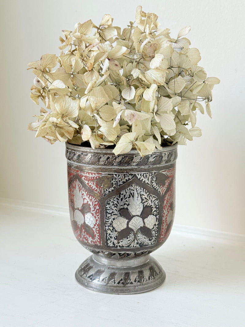 vintage indian metal lassi cup with red and white enamel motifs, styled with dried hydrangeas on a white surface