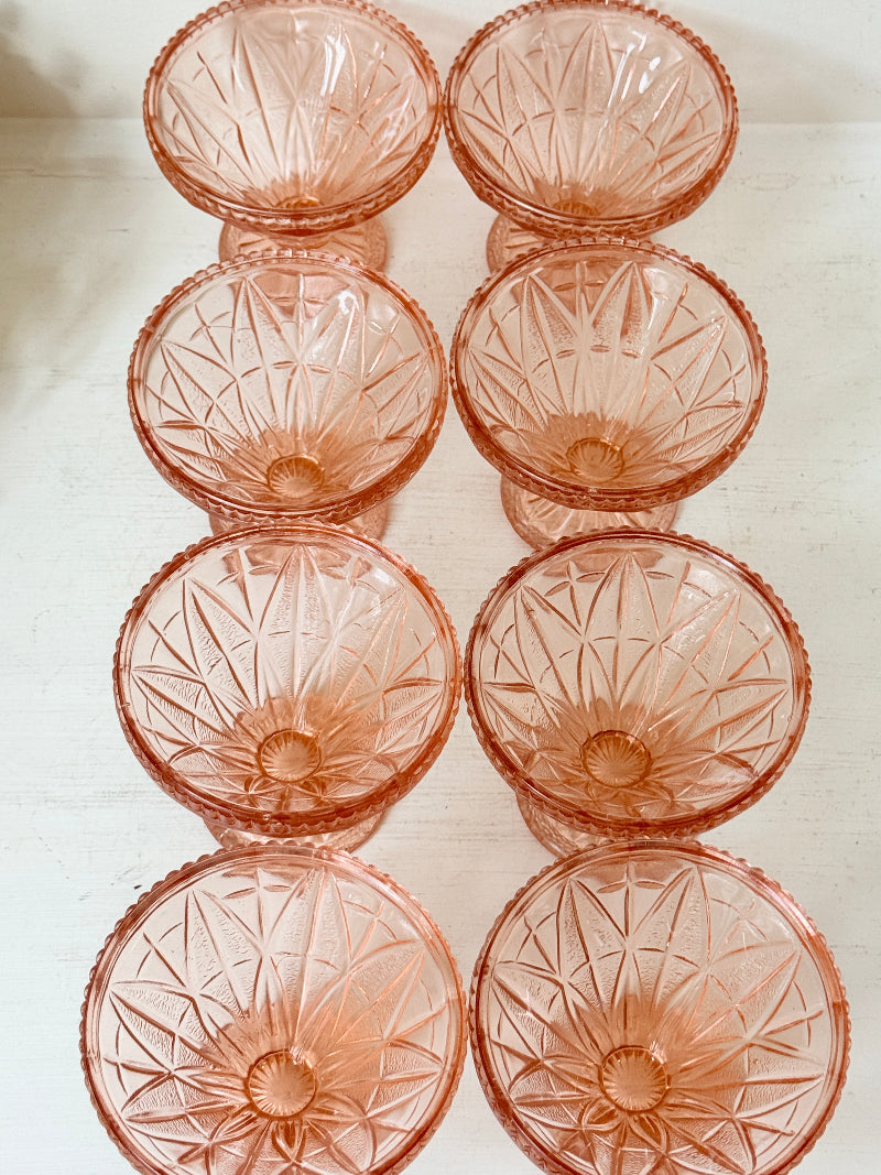 Eight pink cut-glass dessert or cocktail glasses arranged in two columns on a light off-white surface.