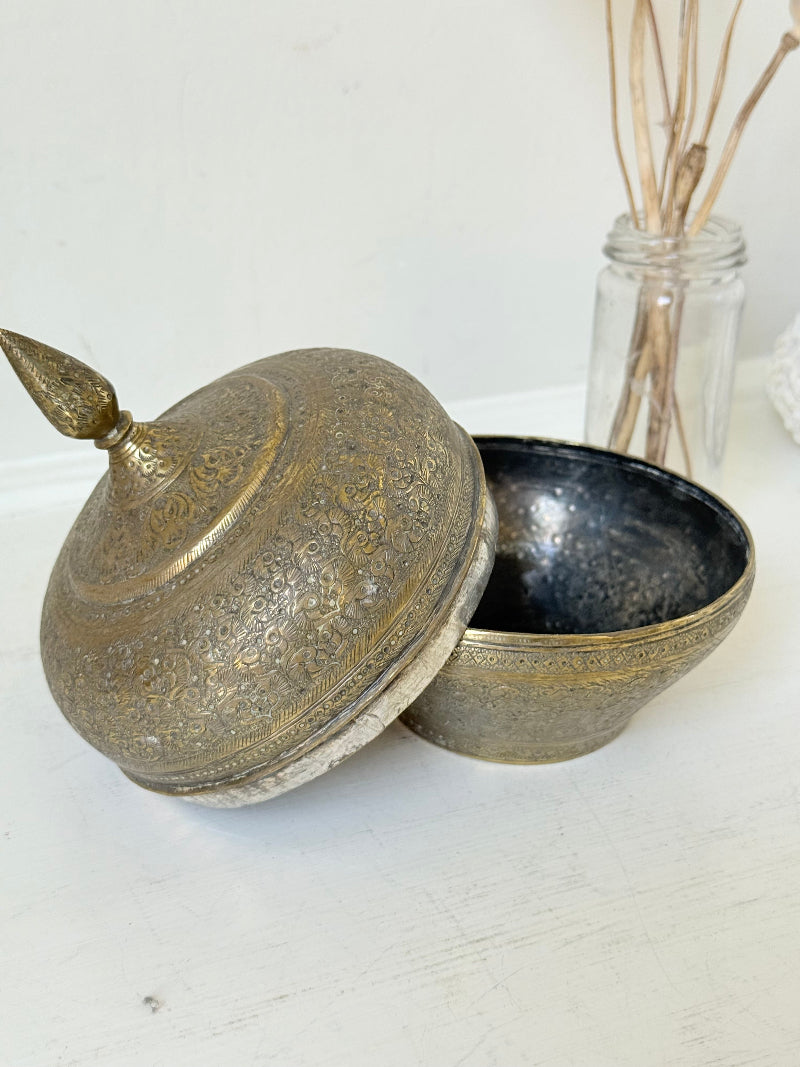 Indian Benares brass lidded jar with pointed finial and darkened interior, photographed on a white surface
