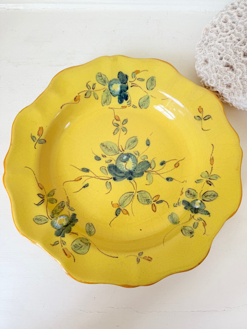 Vintage yellow French faïence plate with scalloped edge and blue floral decoration, photographed on a white surface