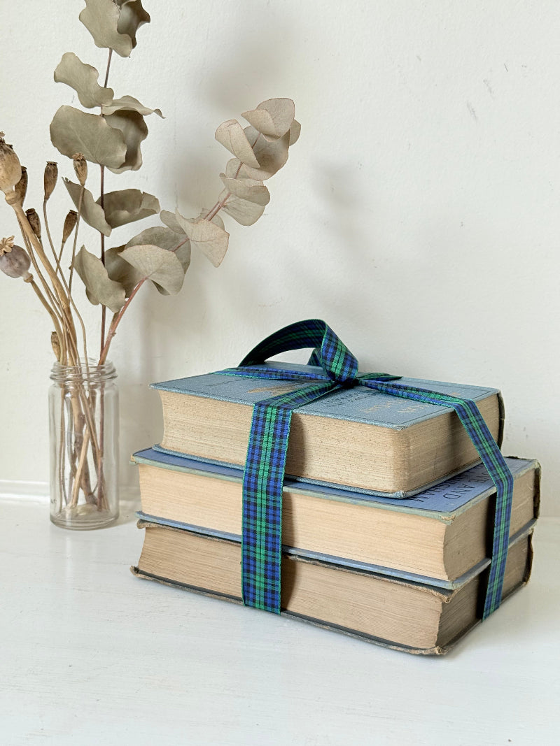 Vintage blue fabric bound decorative book bundle tied with blue and green tartan ribbon, photographed on a white surface