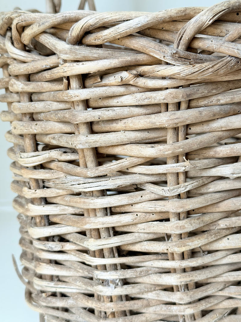 Rustic vintage wicker basket with woven handle and aged natural finish photographed on a white surface