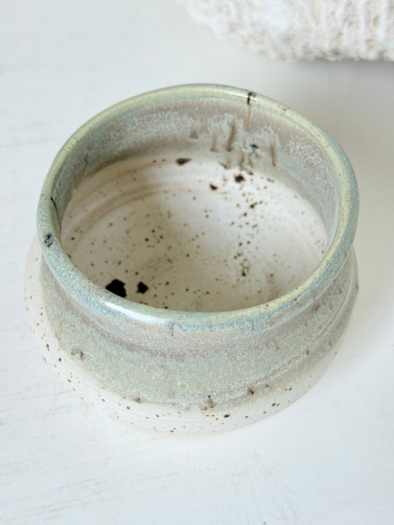 Studio pottery olive pot with soft green and cream glaze, photographed on a white surface