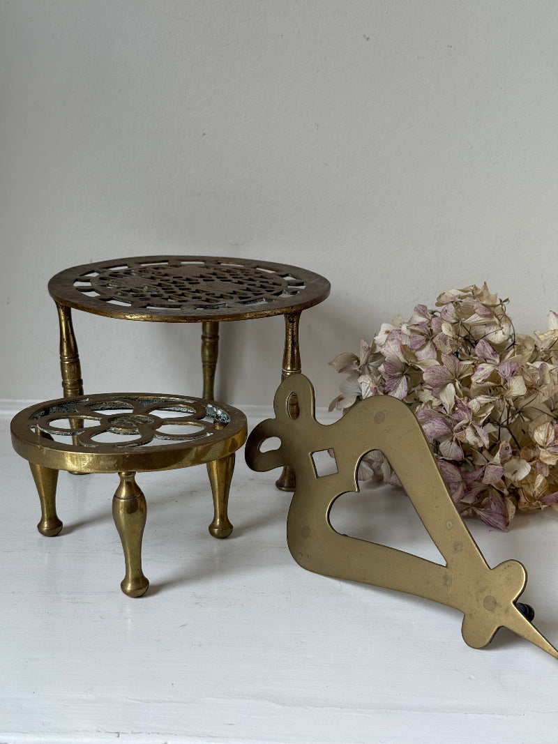 Vintage brass trivet trio with ornate cutwork designs and aged patina, photographed on a white surface