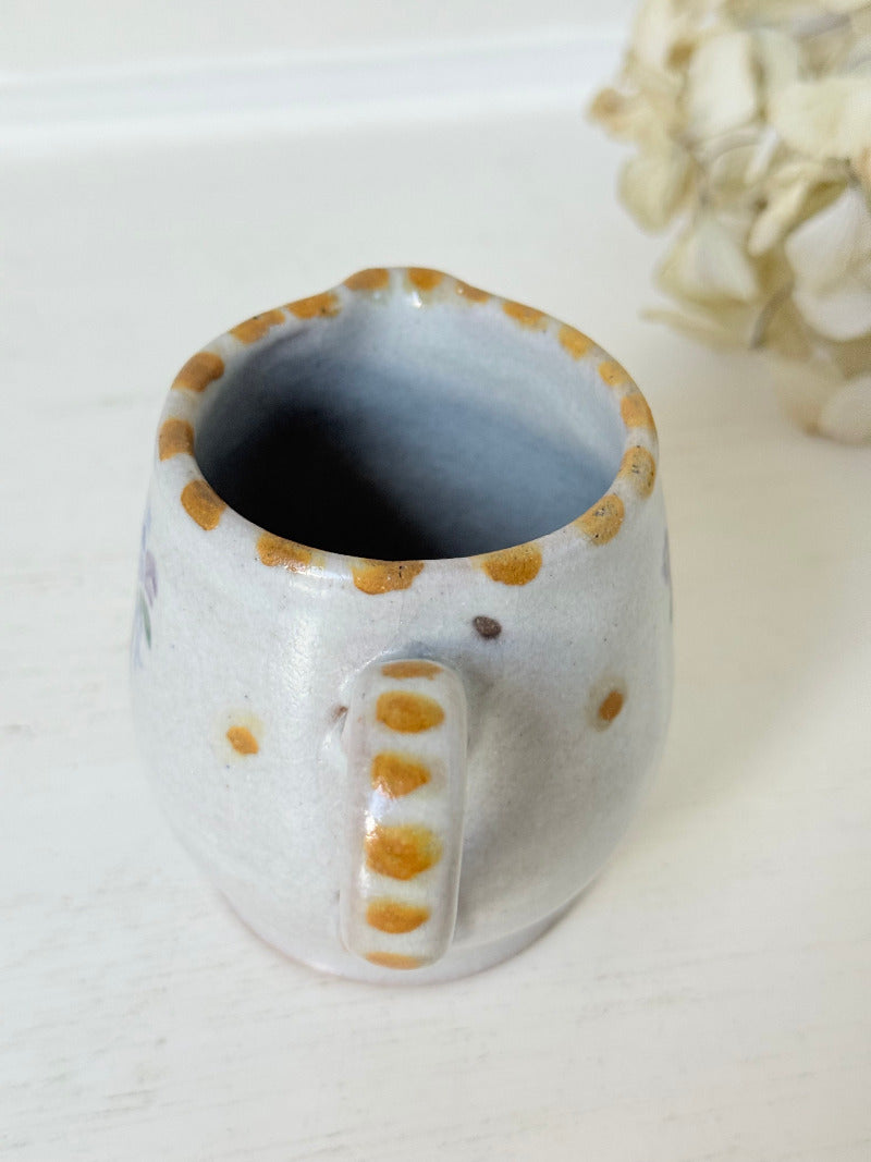 vintage studio pottery milk jug with hand painted lilac flowers and ochre rim photographed on white surface