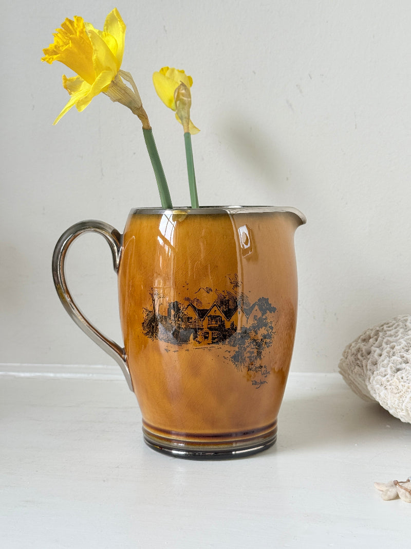 Antique Ridgways stoneware jug photographed on a white surface in amber treacle glaze with black Coaching Days and Coaching Ways transfer scenes and silver tone handle