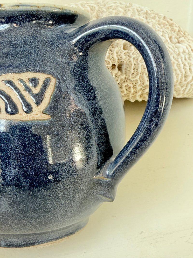 Studio pottery milk jug with deep blue glaze and cream geometric band, photographed on a white surface