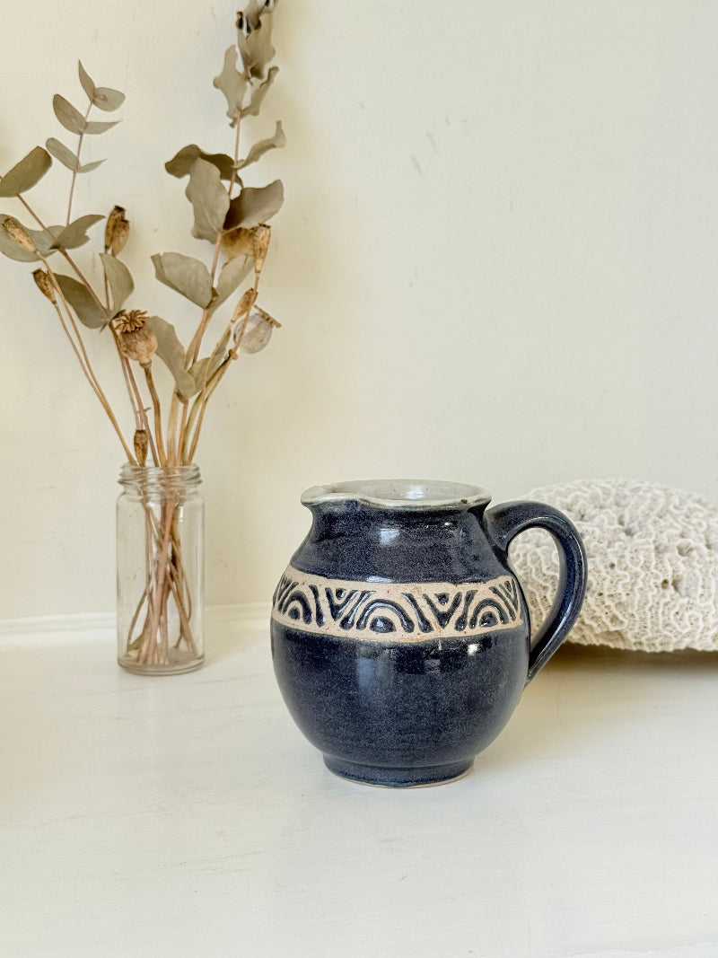 Studio pottery milk jug with deep blue glaze and cream geometric band, photographed on a white surface