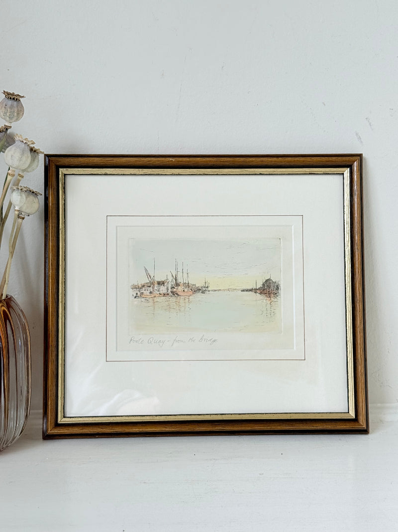 Framed vintage print of Poole Quay harbour scene in muted tones, under glass with gilt and wood-effect frame, on white surface.