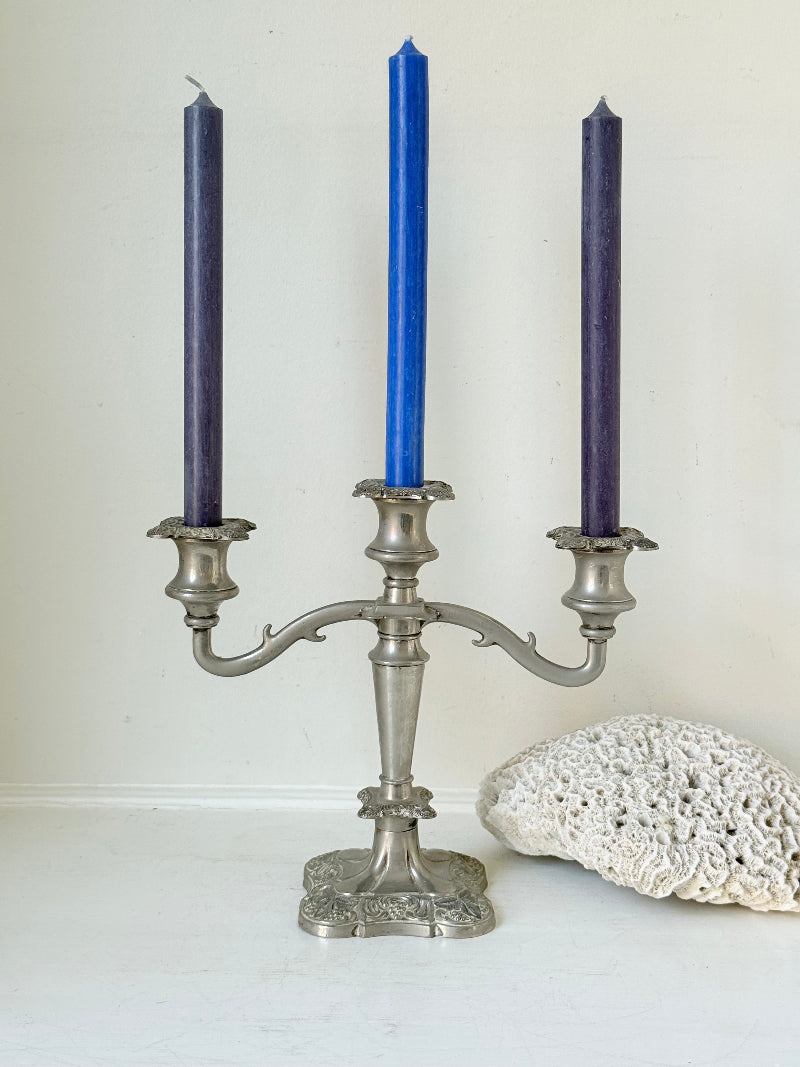 Vintage silver coloured three-arm candelabra with ornate base and soft patina, photographed on a white surface