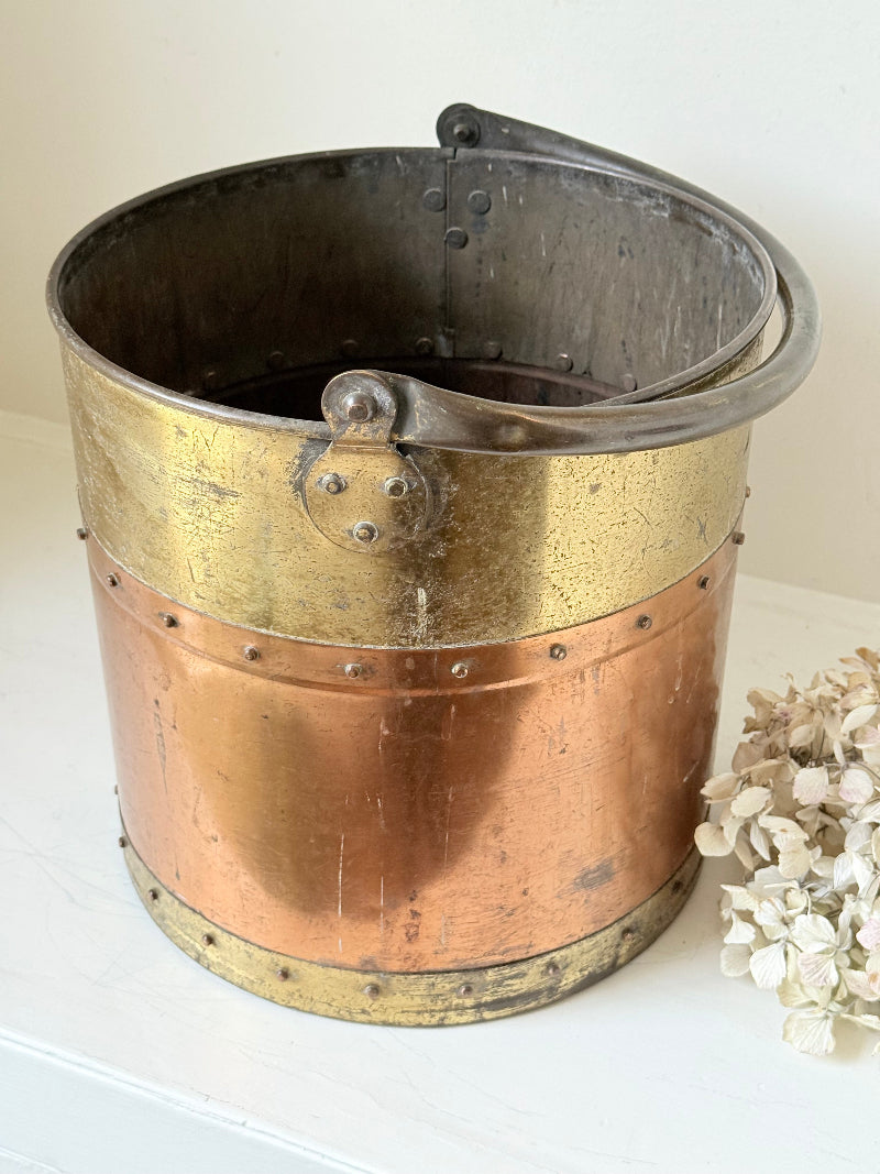 Vintage copper and brass metal bin with handle, photographed on a white surface.
