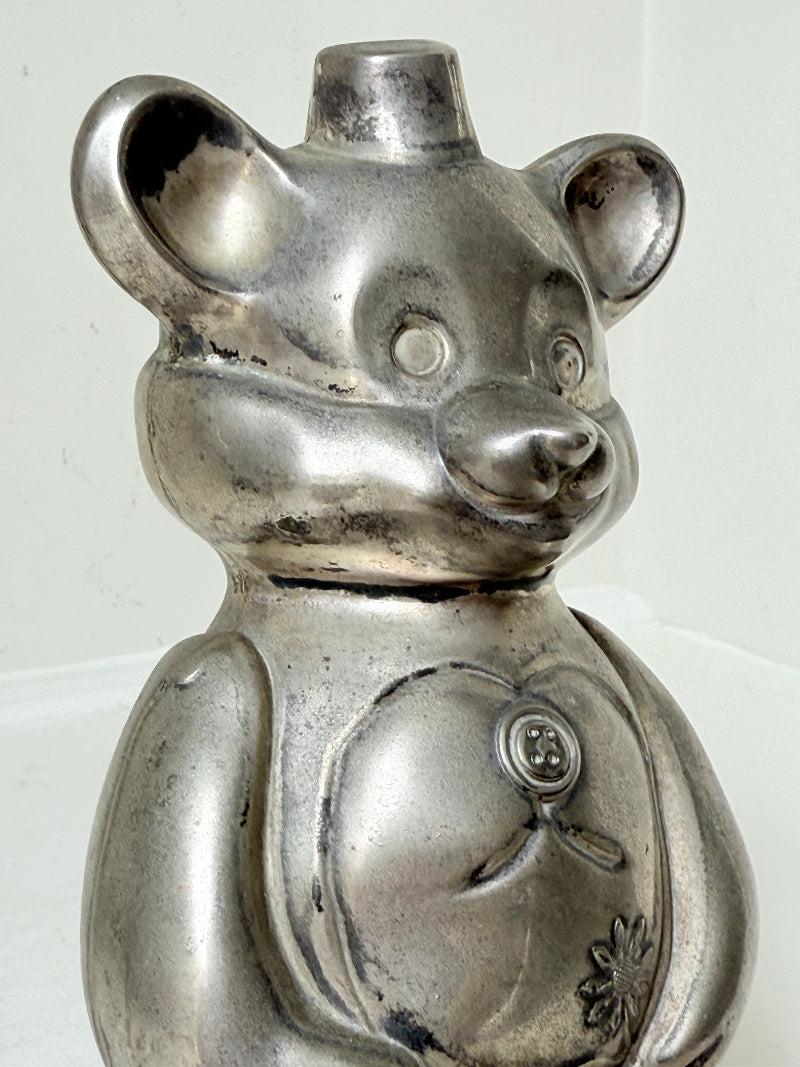 Vintage silver tone metal bear money box with coin slot on top, photographed on a white surface.