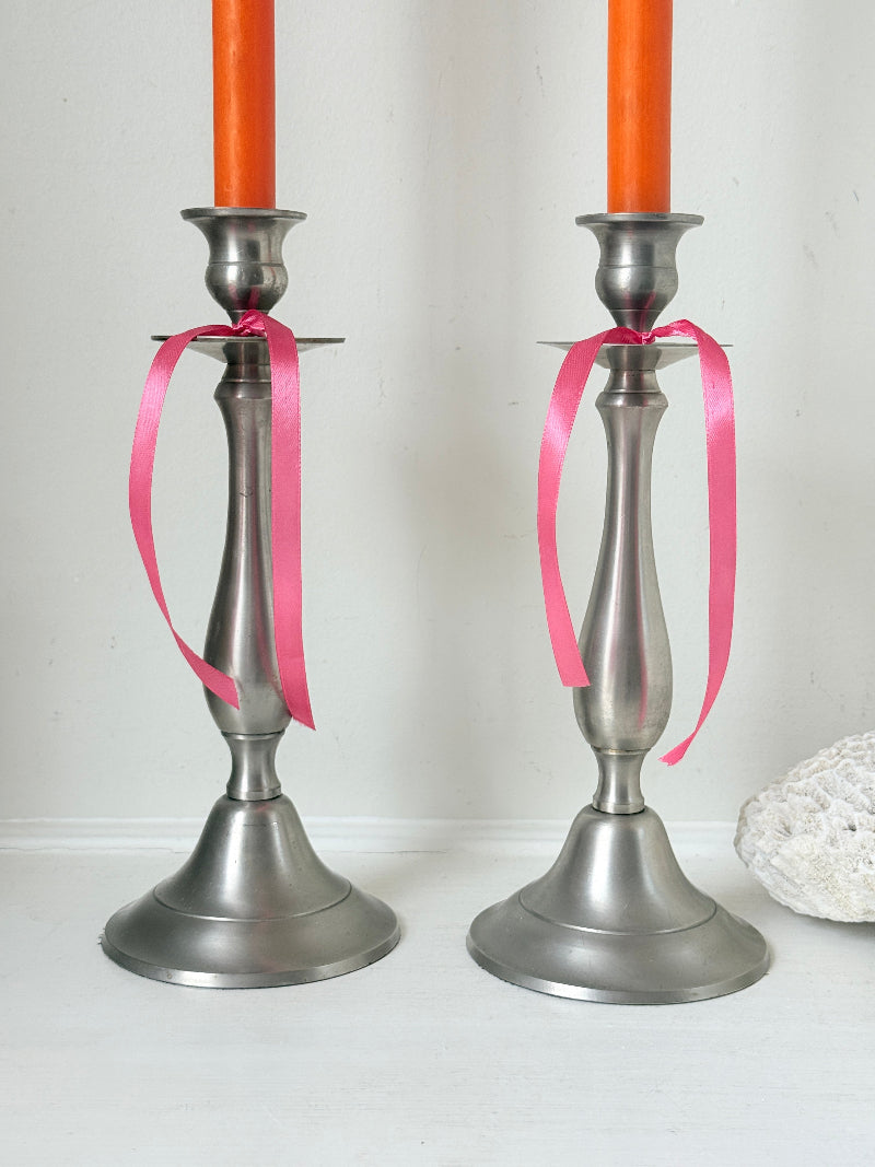 Pair of vintage pewter effect baluster candlesticks with orange taper candles styled on a white surface