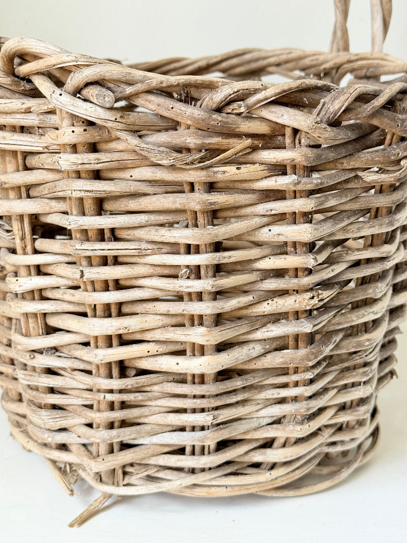 Rustic vintage wicker basket with woven handle and aged natural finish photographed on a white surface