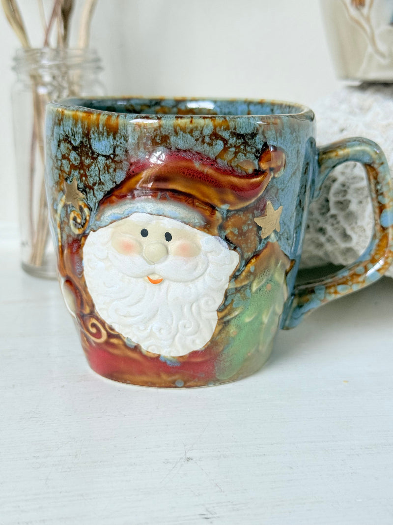 Pair of Christmas mugs with Santa and snowman designs photographed on a white surface.