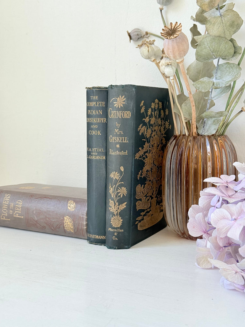 Bundle of antique books with decorative spines tied with ribbon, styled on white surface with dried flowers