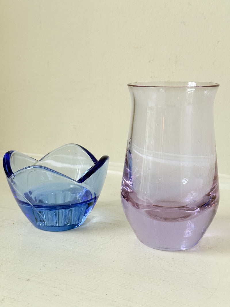 Blue Bormioli Rocco glass candlestick and lilac glass vase photographed on a white surface
