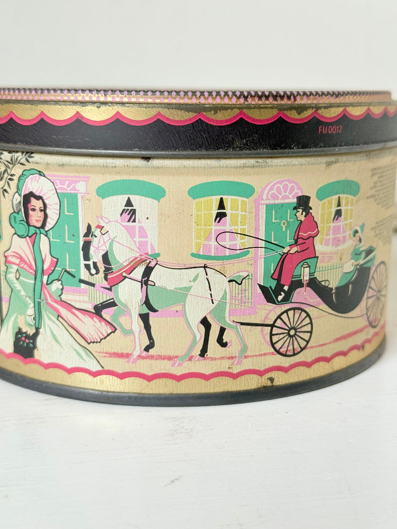 Vintage Quality Street tin from 1986 with colourful illustrated street scenes and pastel design, photographed on a white surface.
