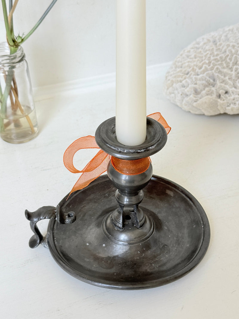 Vintage pewter chamberstick with handle and circular tray, photographed on a white surface