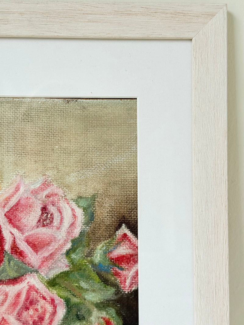 Framed original rose still life painting in pink and yellow, photographed on a white surface.