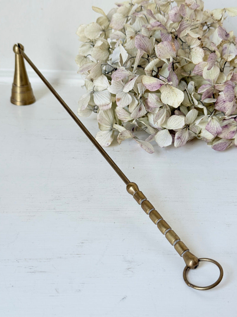 vintage brass candle snuffer with twisted handle and cone-shaped head photographed on white surface