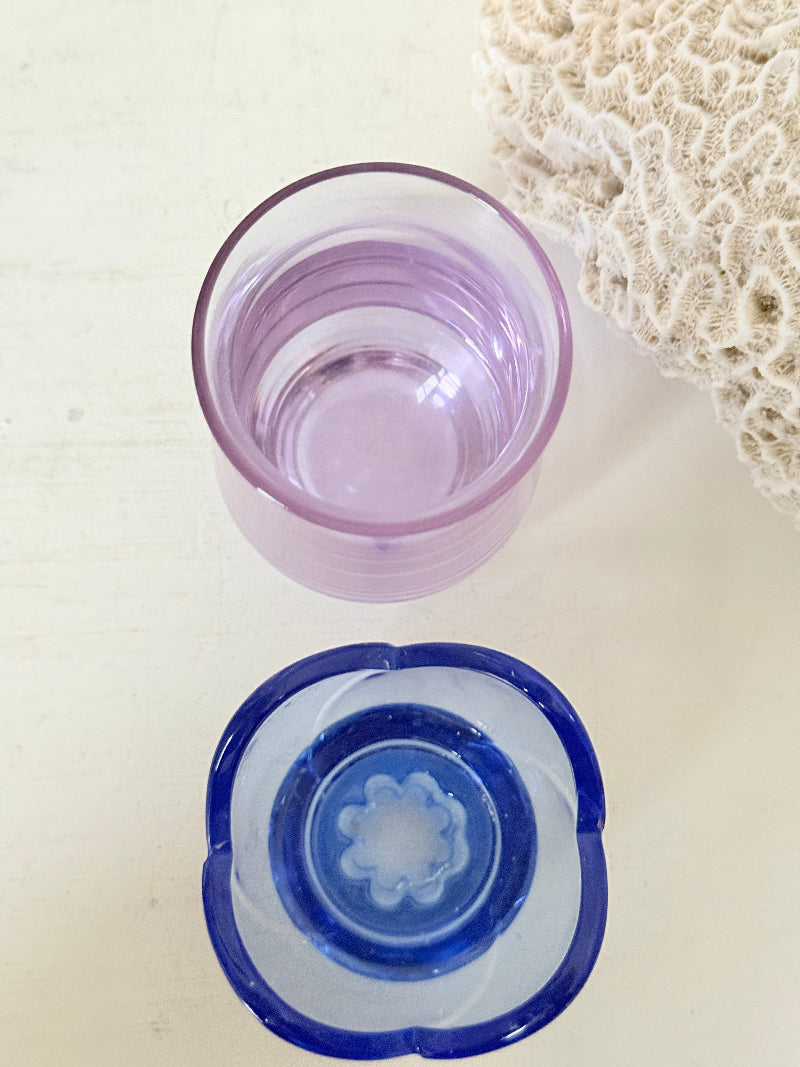 Blue Bormioli Rocco glass candlestick and lilac glass vase photographed on a white surface