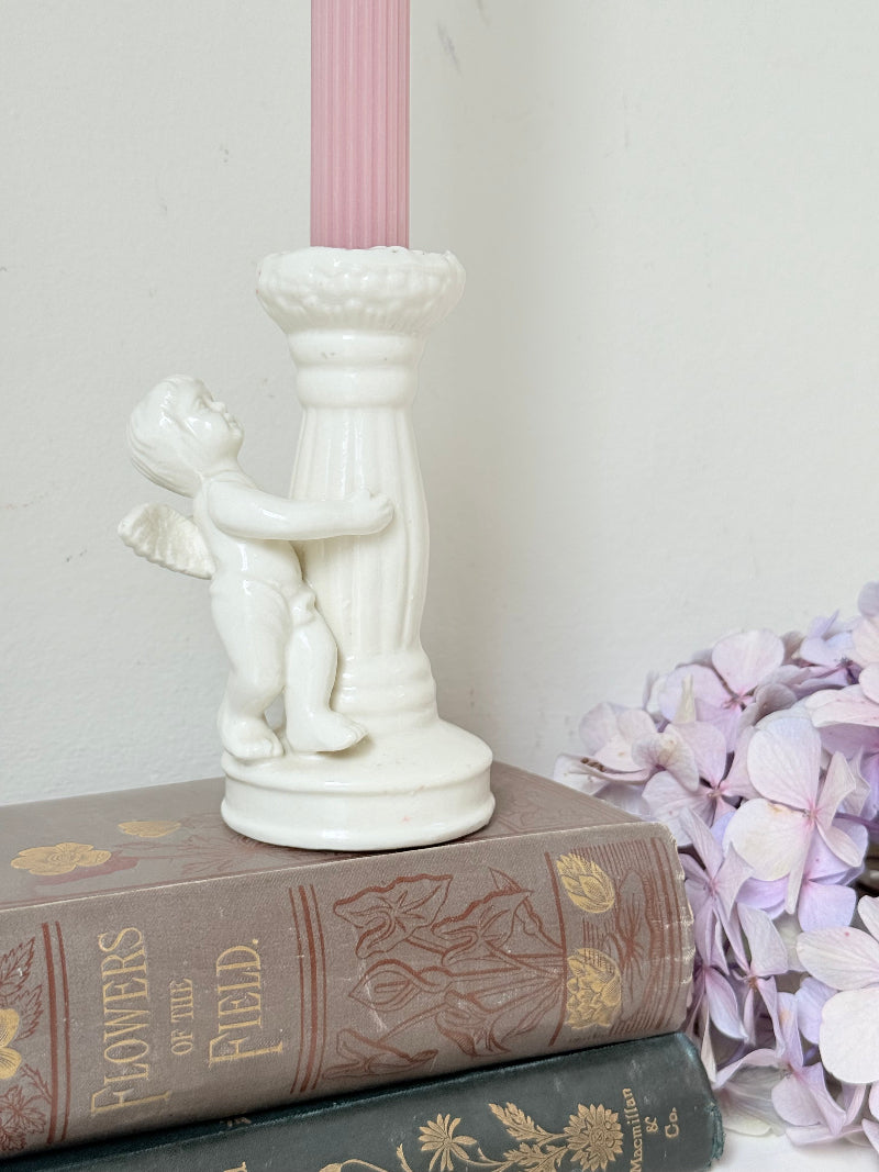 Vintage ceramic candlestick with angel figure and fluted column, cream glazed, styled with pink candle on white surface