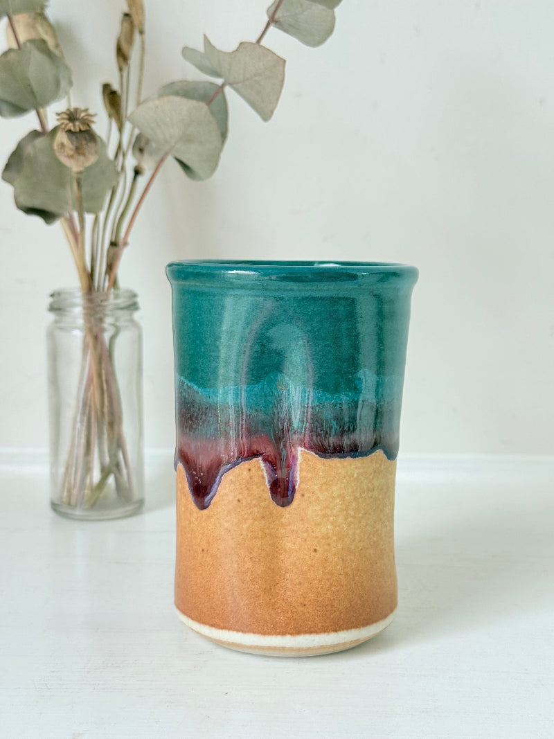 Studio pottery pen pot with teal and plum drip glaze, photographed on a white surface