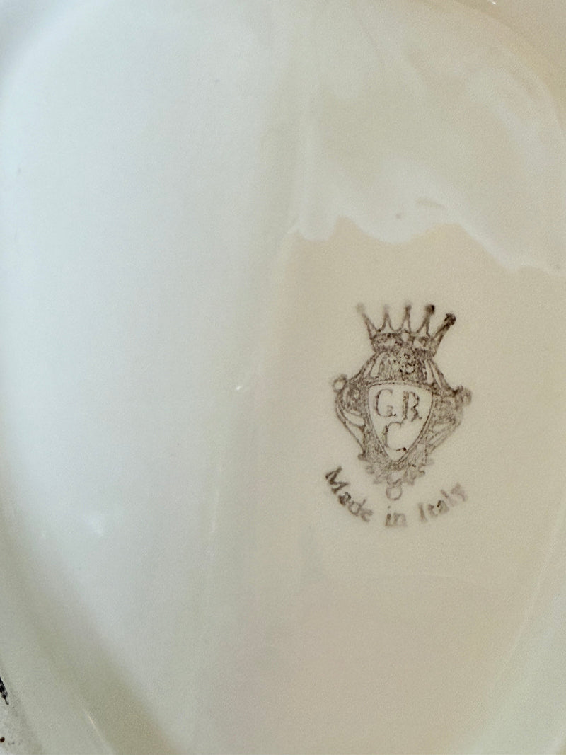 Italian ceramic dish featuring two white dogs on a sculpted leaf base, photographed on a white surface.