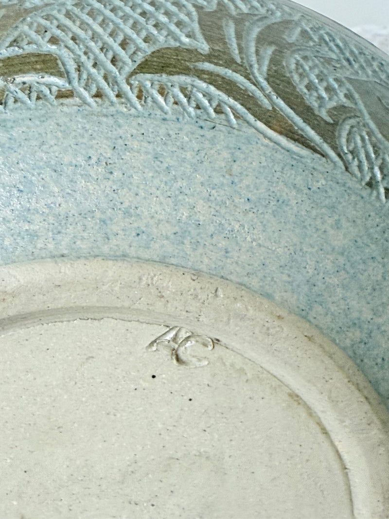 Studio pottery bowl with carved floral and geometric decoration in neutral glaze, photographed on a white surface with a pear inside.