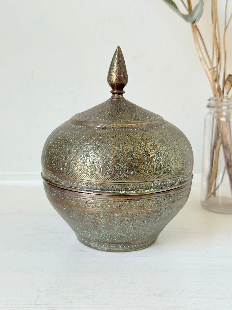 Indian Benares brass lidded jar with floral engraving and finial, photographed on a white surface