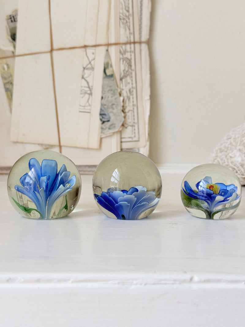 Trio of vintage glass paperweights with hand worked blue floral detail, clear glass domes and green leaf decoration
