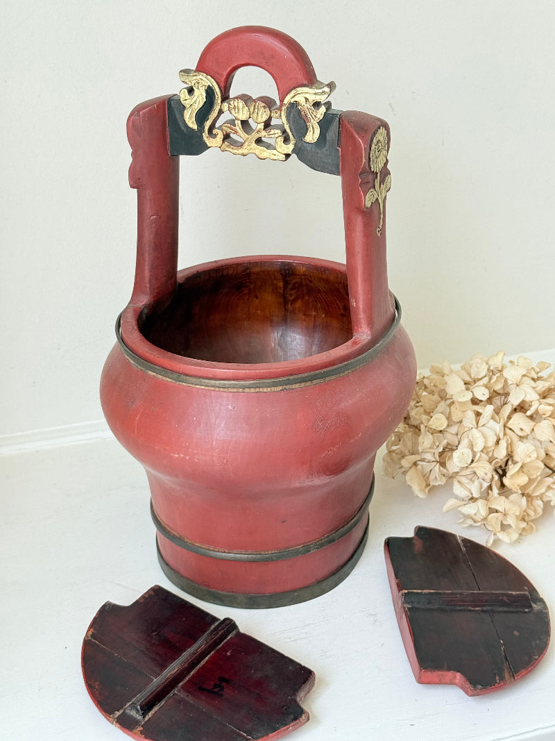 Vintage red painted wooden basket with upright handle and gold painted detail photographed on a white surface