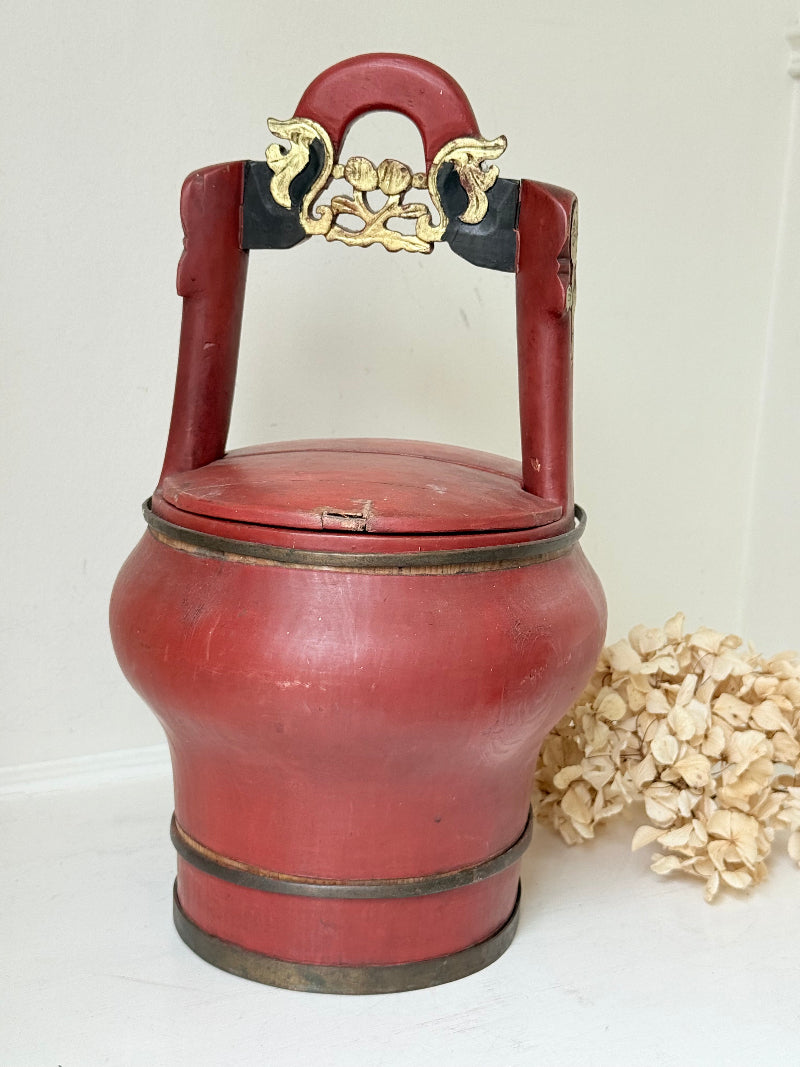 Vintage red painted wooden basket with upright handle and gold painted detail photographed on a white surface