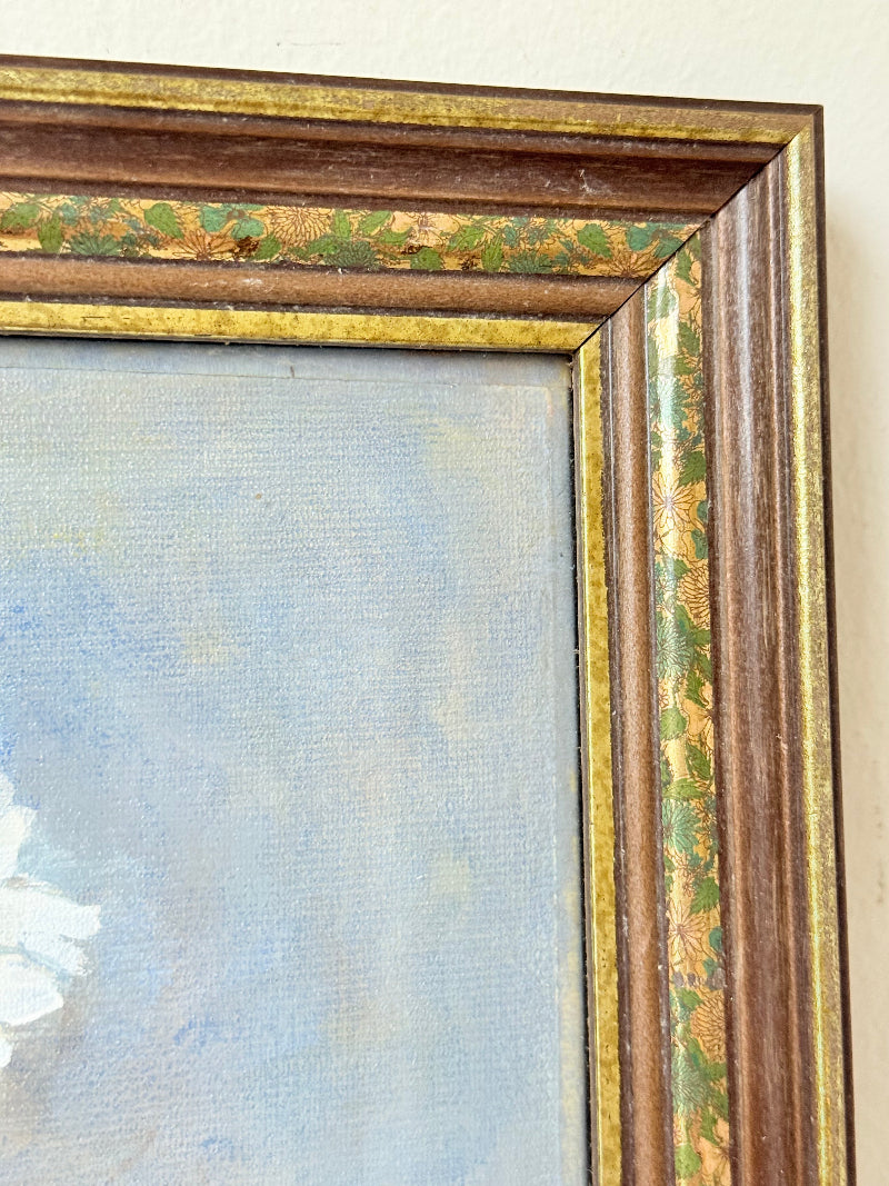 Vintage oil painting on board of daisies in a vase, framed under glass and photographed on a white surface beside dried flowers.