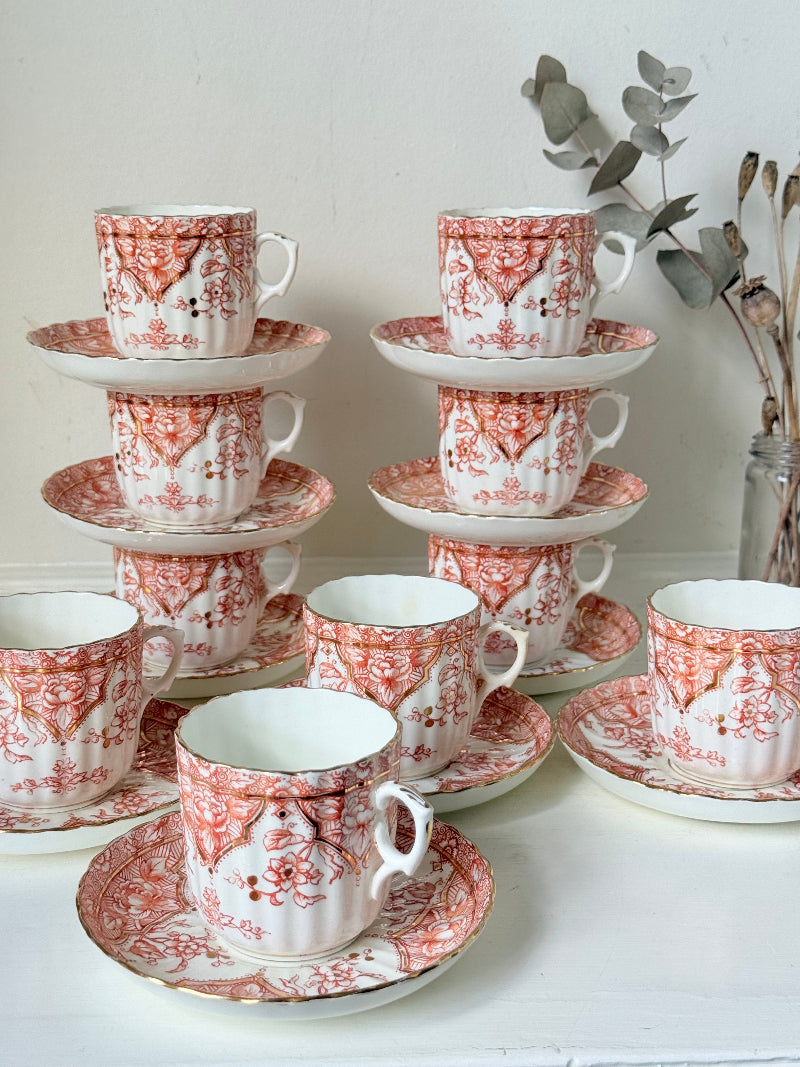 Vintage coral transferware coffee cans and saucers with scalloped edges and gold accents, set of ten, styled on a white surface.